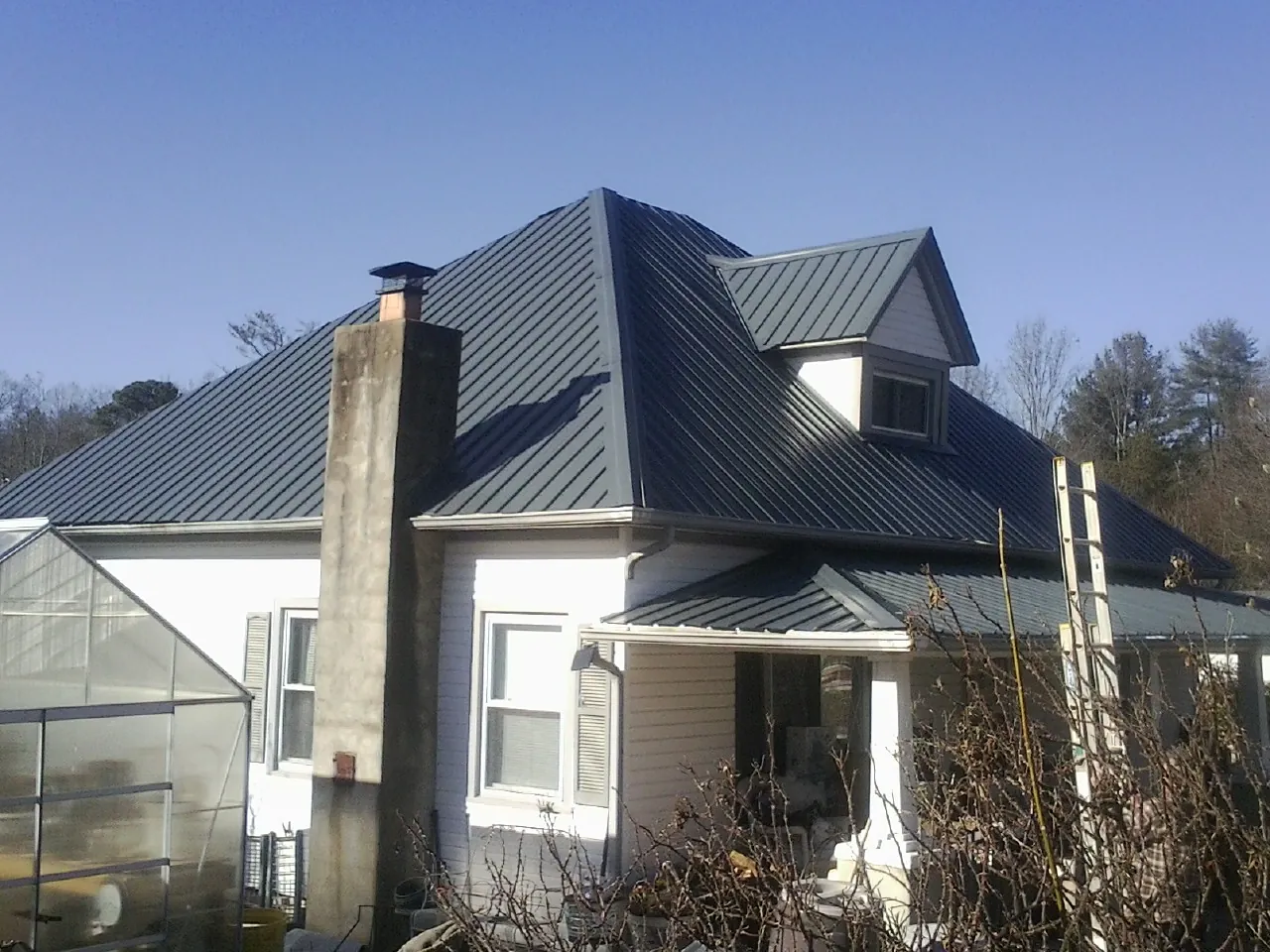 Dark blue standing seam metal roof on a white farmhouse with dormer — Slate & Tile Roof Repair by Roofing Brothers in Usaf Academy