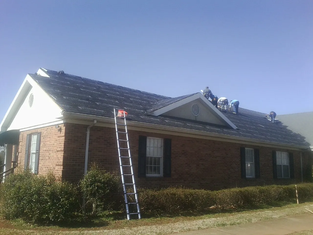 Crew tearing shingles off a brick ranch roof with a ladder set — Emergency Roof Repair work by our crew in Usaf Academy