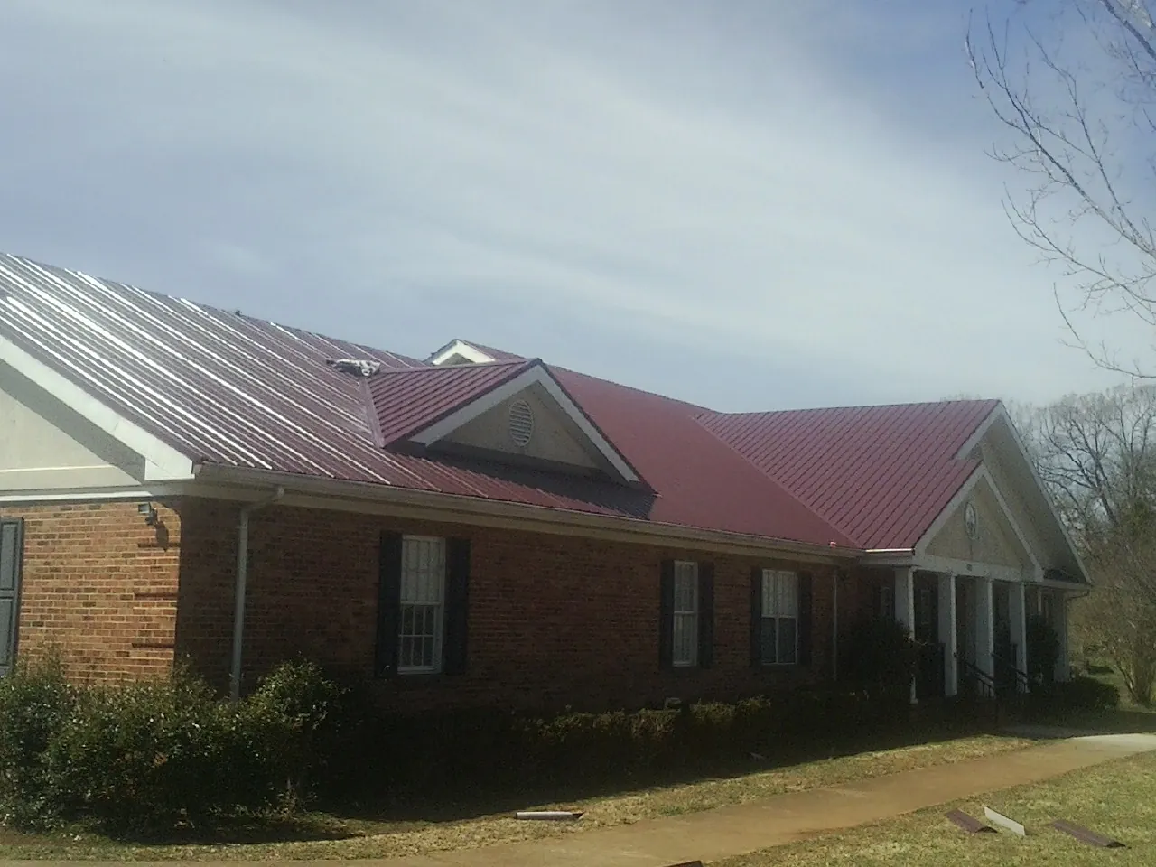 Red metal roof with gabled entries on a long brick building, from a Hail Damage Roof Repair job in Usaf Academy