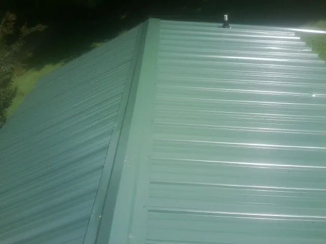 New green metal panels meeting at the ridge of a roof — Flat Roof Repair work by our crew in Usaf Academy