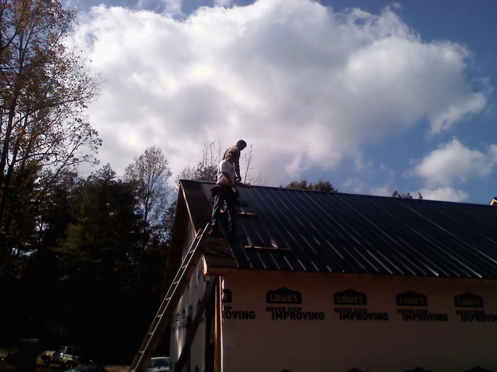 Roofer fastening dark metal panels high against a cloudy sky, from a Roof Inspection job in Usaf Academy
