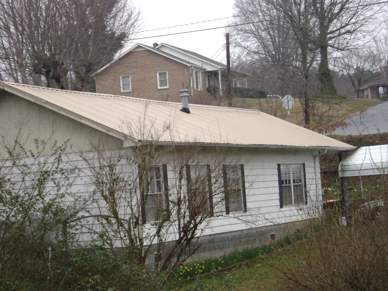 Tan metal roof on a white sided house set into a hillside — Commercial Roofing by Roofing Brothers in Usaf Academy